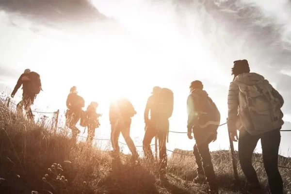 Un gruppo di escursionisti cammina in salita verso il sole al tramonto.